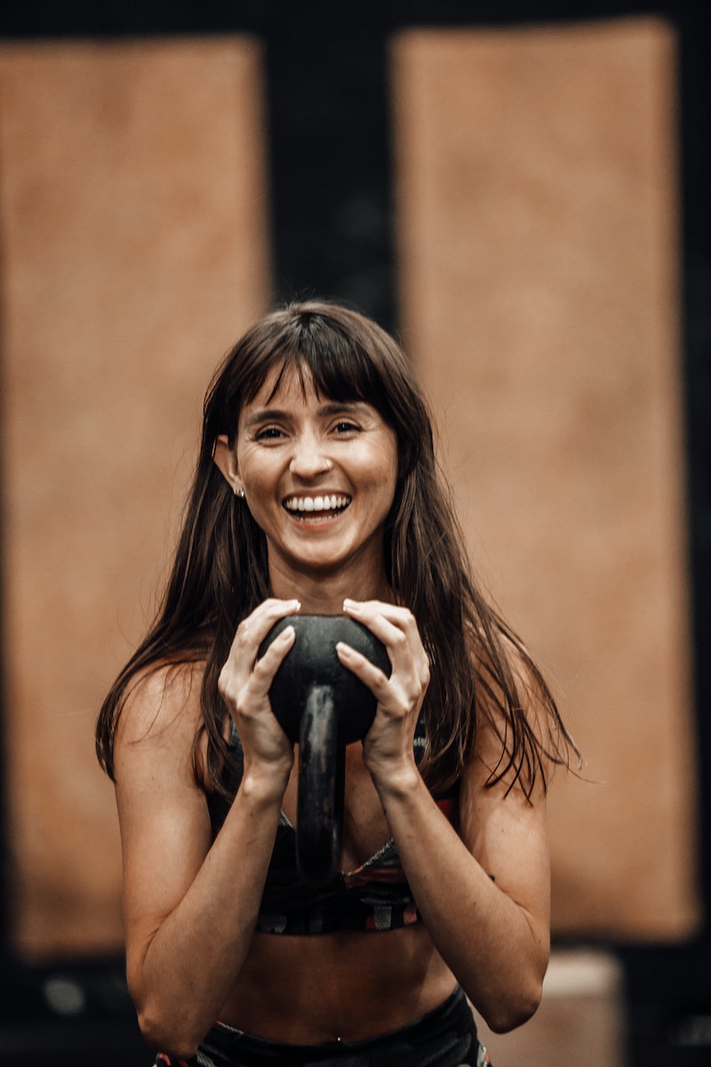 Portrait of a Young Brunette Laughing while Exercising with a Kettlebell